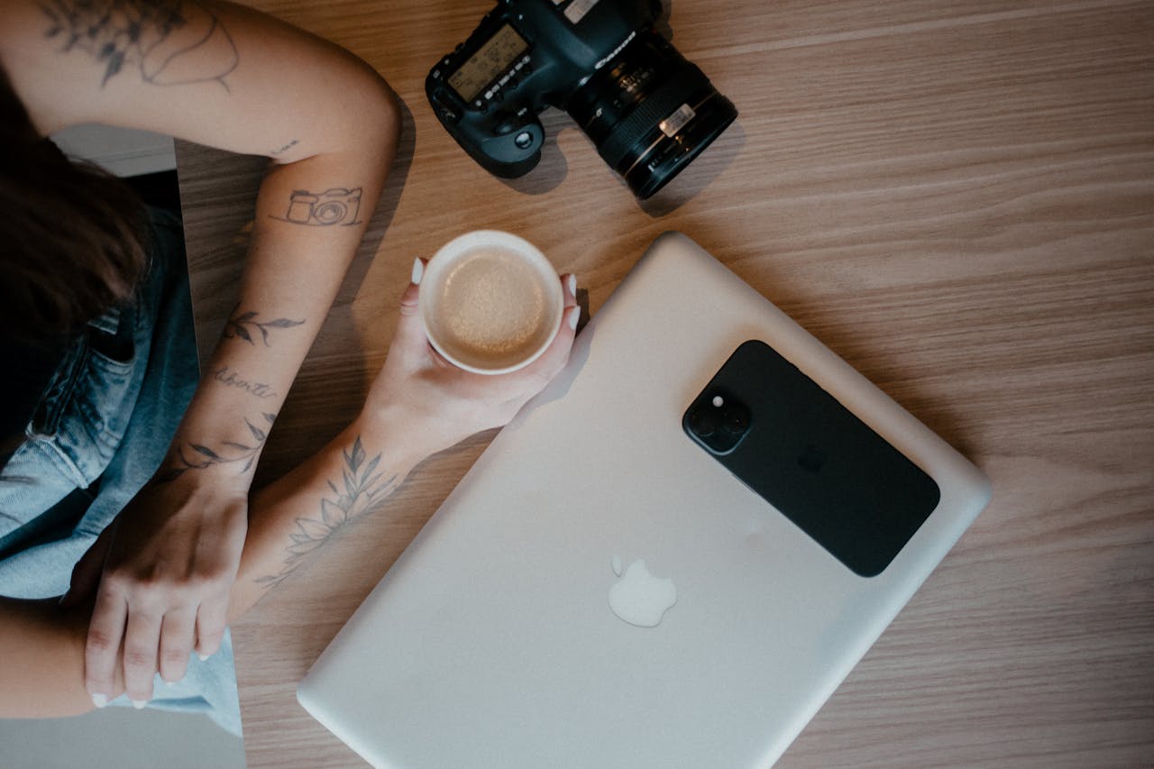 A cozy creative workspace setting with a laptop, camera, and coffee cup.